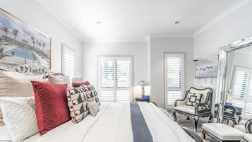 A bedroom with a large bed, two windows with blinds, a chair, and a mirror.