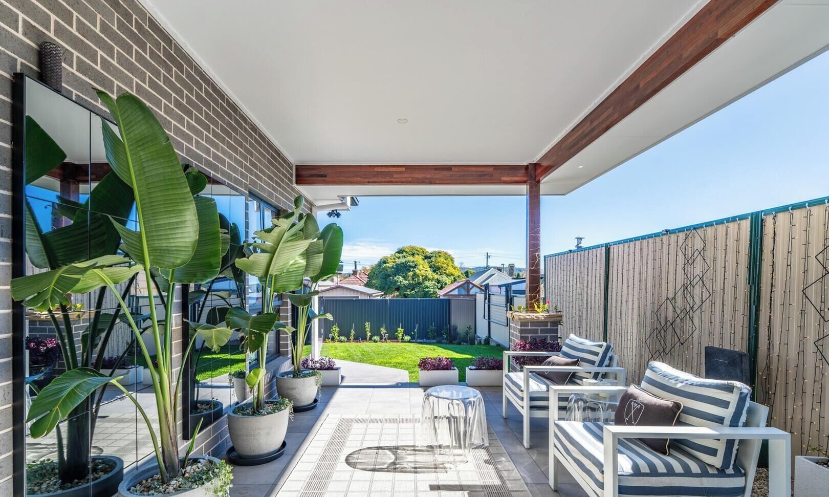 A covered patio with outdoor furniture, potted plants, and a view of the backyard.