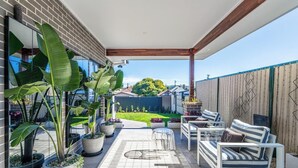 Un patio techado con mobiliario exterior, plantas en macetas y vistas al jardín trasero.