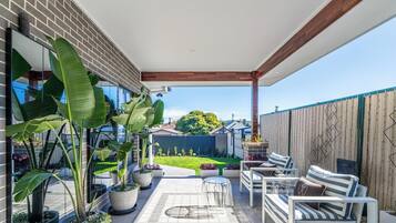A covered patio with outdoor furniture, potted plants, and a view of the backyard.