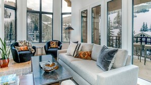 A modern living room with a sofa, armchairs, and a coffee table. Large windows offer views of a snowy landscape. - Gorgeous 4 Bedroom Ski In/out Condo in Beaver Creek Village (Avon)