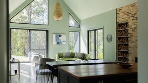 A spacious living area with large windows, a green sofa, a dining table, and a brick fireplace. - Balangara, Exeter, Southern Highlands (Exeter)