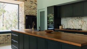 A modern kitchen with dark cabinetry, a brick accent wall, a wooden countertop, and a marble backsplash. - Balangara, Exeter, Southern Highlands (Exeter)