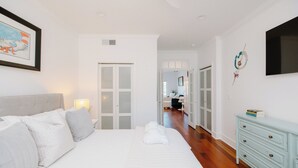 A bedroom with a bed, bedside table, and a dresser. There is a door leading to another room.