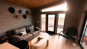Ein modernes Wohnzimmer mit Ledersofa, rundem Couchtisch und Blick durch große Glasfenstertüren in einen Außenbereich.