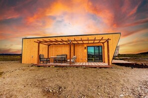 Una cabaña moderna de madera con un porche cubierto, dos sofás y una mesa.