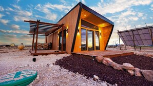 Eine moderne Holzhütte mit einer Terrasse, großen Fenstern und Solaranlagen.