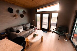 Una sala de estar moderna con un sofá de cuero, una mesa de centro redonda y vistas a un área exterior a través de puertas de vidrio amplias.