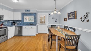 Een keuken met witte kasten, een blauwe spatwand en een houten eettafel met stoelen.