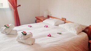 A neatly made bed with white linens and pink flowers, a wooden nightstand with a lamp, and a window with curtains. - Los Angeles 1 bedroom pool view 520 (ARONA)