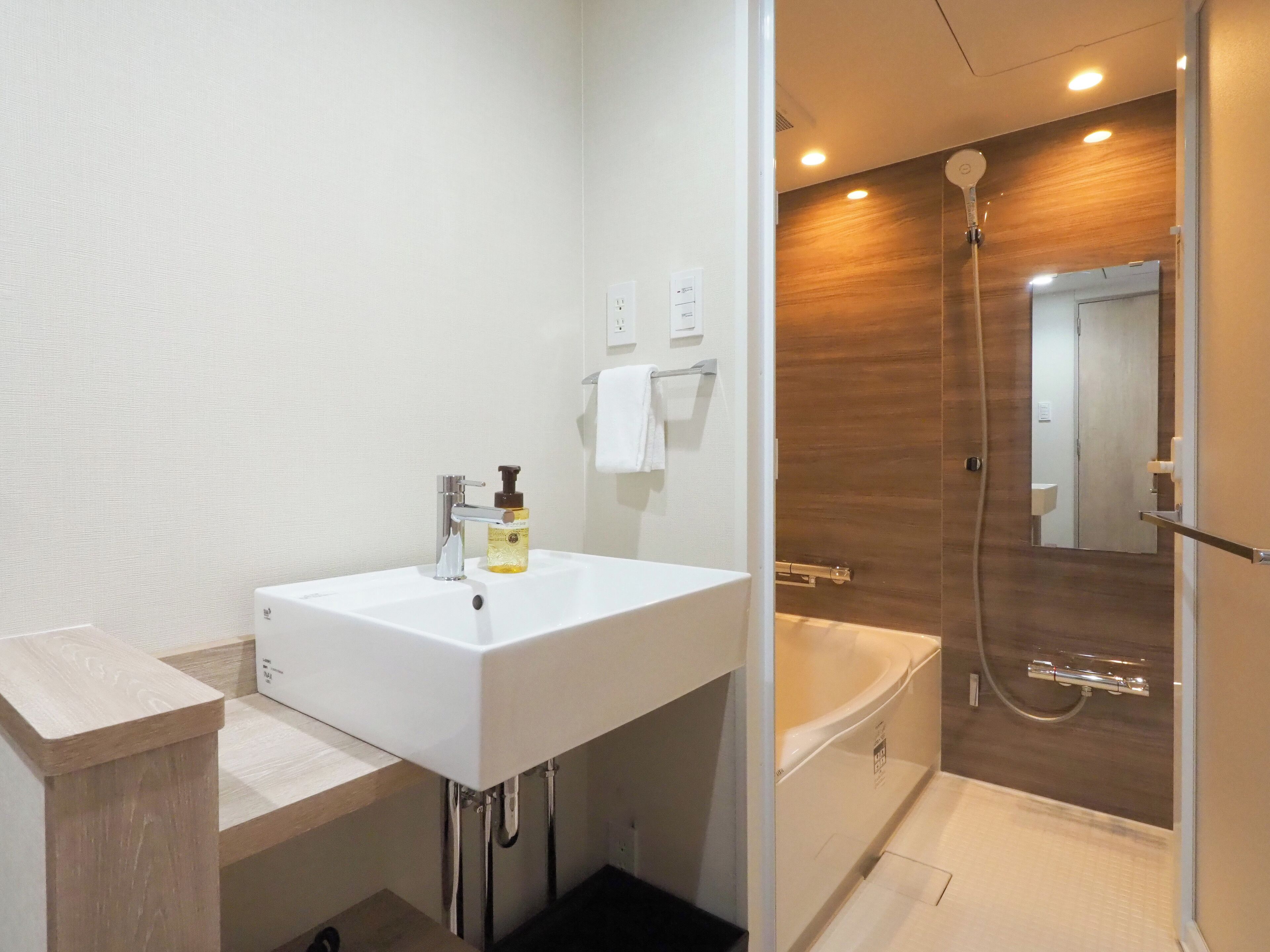 A modern bathroom with a white sink, a shower, and a wooden vanity.