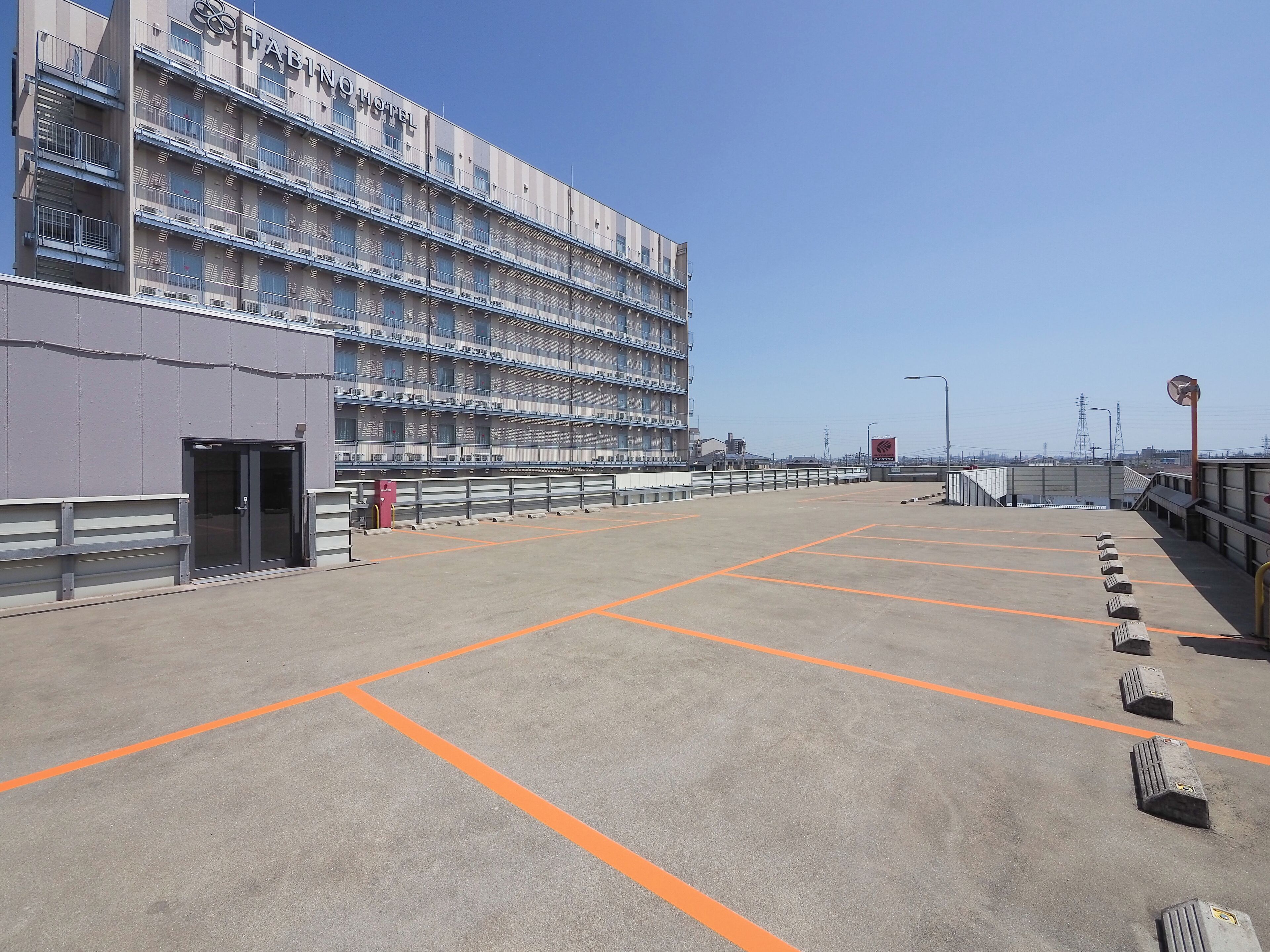 Un hotel con diversi piani e balconi, un'area di parcheggio con strisce arancioni e un cielo sereno.