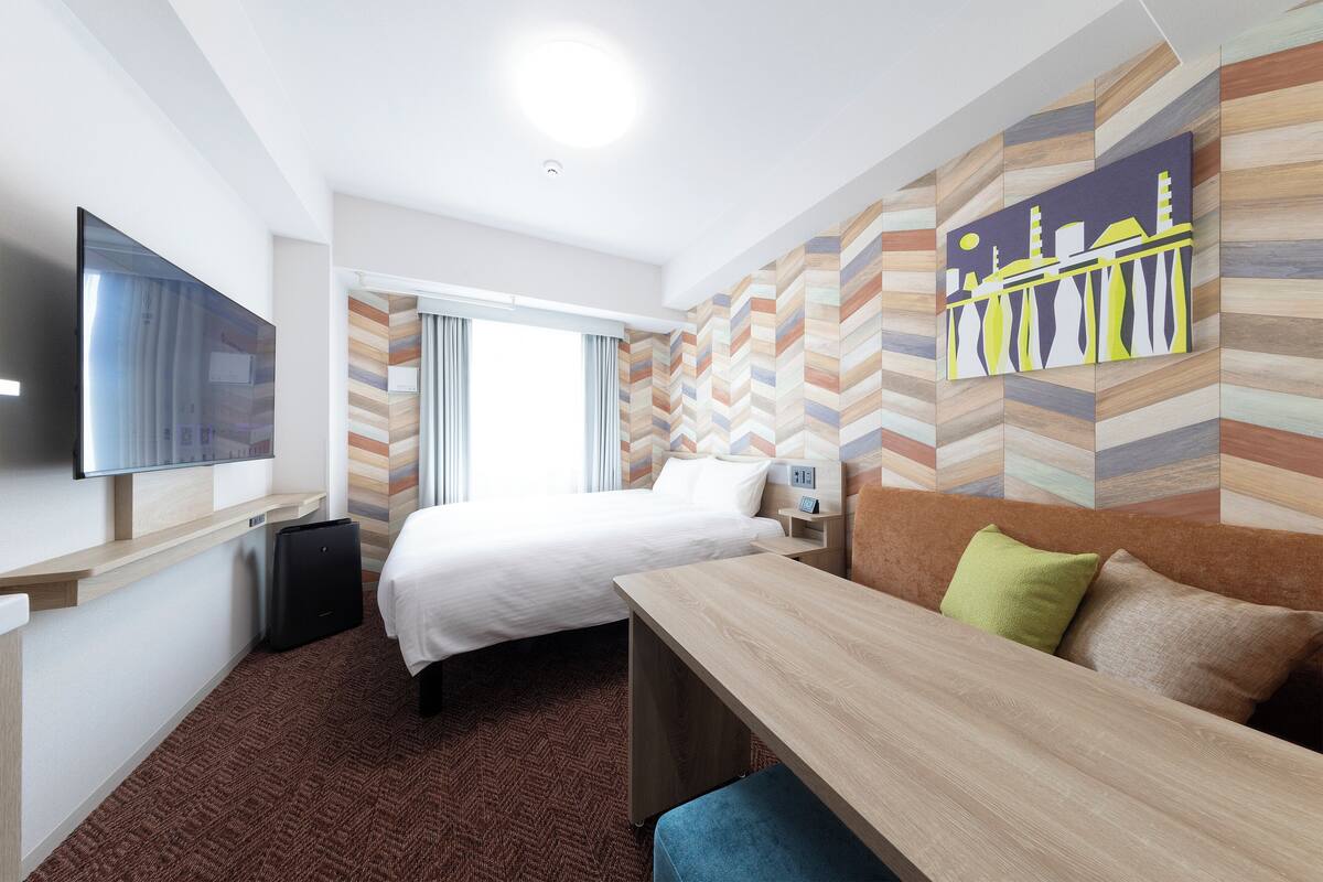 Ein Hotelzimmer mit Bett, Schreibtisch, Flachbildfernseher und Wand mit geometrischem Muster.