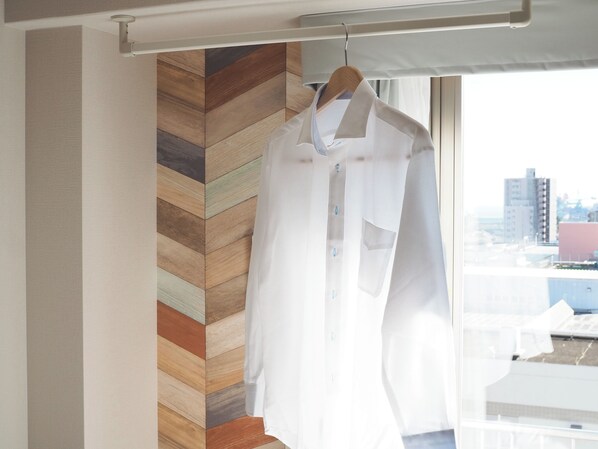 Una camisa blanca colgada en una percha de madera en una habitación con un papel tapiz de espiga y una ventana con vistas a edificios.
