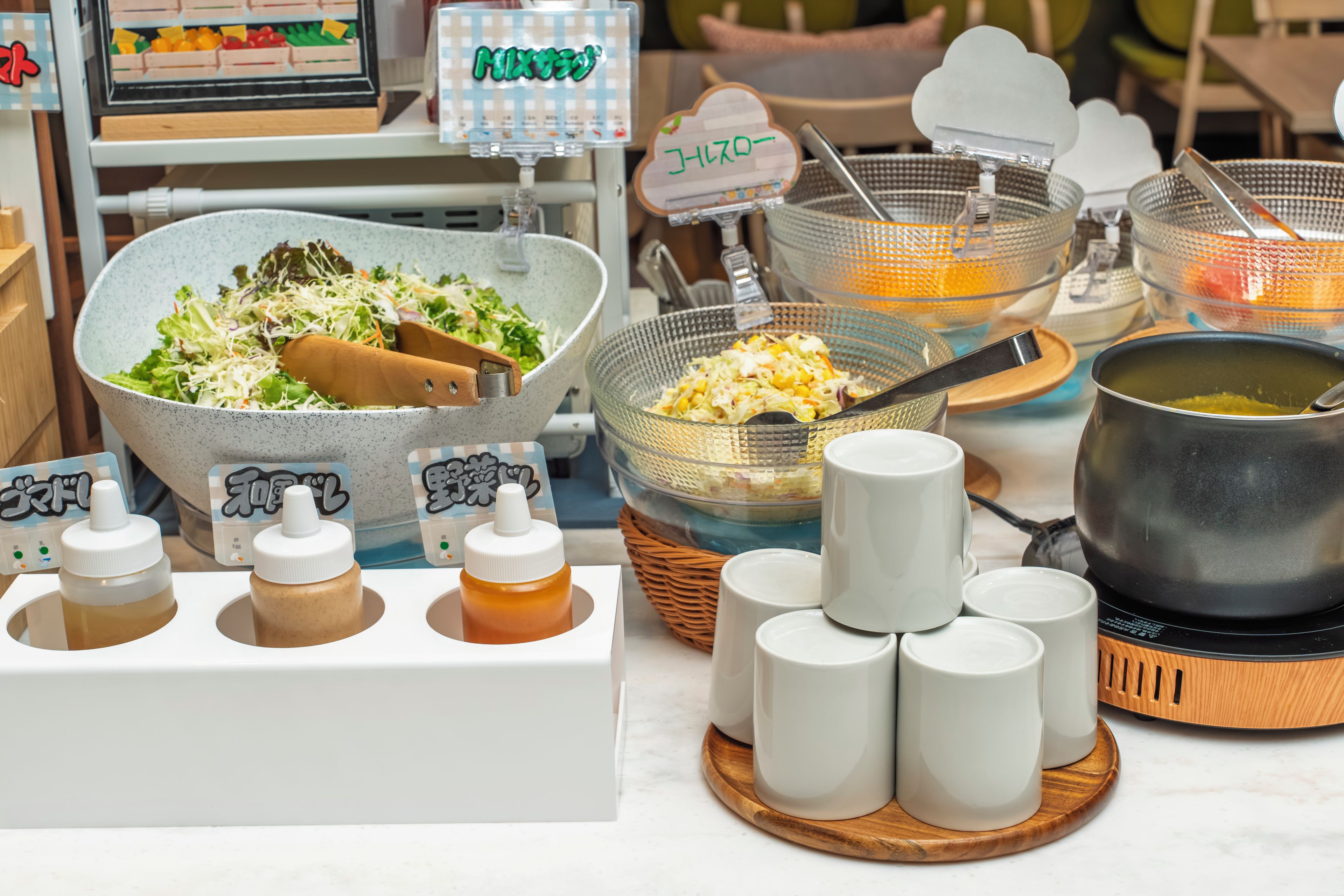 A variety of food items and condiments, including a bowl of salad, a colander with vegetables, and several condiment bottles.