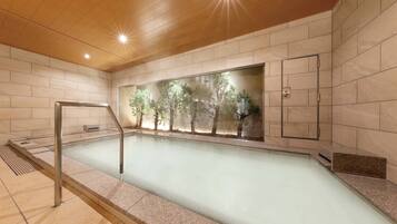 A modern indoor swimming pool with clear glass walls, wooden ceiling, and tiled floors.