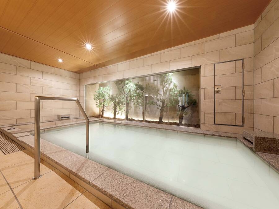 A modern indoor swimming pool with clear glass walls, wooden ceiling, and tiled floors.