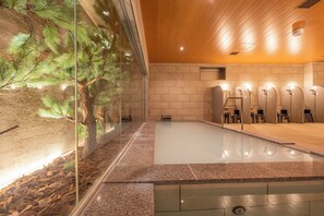 Un espace piscine intérieur moderne, doté d’un mur en verre, d’un plafond en bois et d’un mur en pierre avec un sauna intégré.