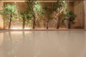 Un bassin aux eaux calmes, avec en arrière-plan des arbres artificiels et un mur à texture particulière.