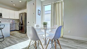 Une cuisine moderne avec des meubles blancs, un réfrigérateur en acier inoxydable et un coin repas comprenant une table ronde et quatre chaises.
