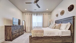 Une chambre à coucher avec un lit en bois, une télévision, une commode et un ventilateur de plafond.