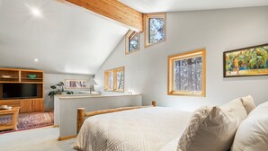 Quarto com cama grande, televisão, escrivaninha e janela com vista para árvores.