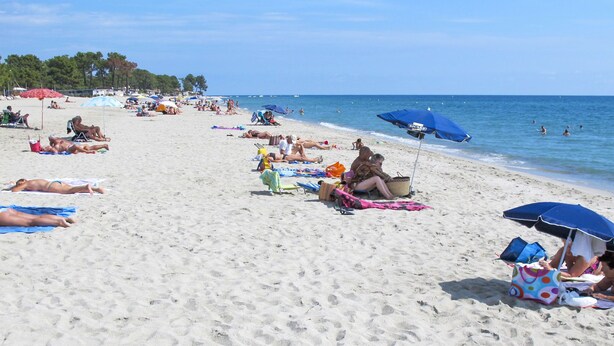 Una playa con gente tomando el sol y nadando.