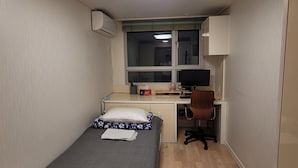 Una habitación pequeña y estrecha con una cama, un escritorio, una silla y un ventanal.