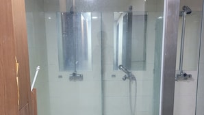 Un box de ducha con paredes de vidrio, con ducha y panel de control a la vista.