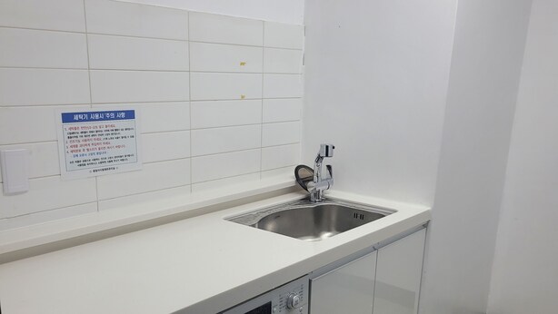 Zona de lavandería con lavadora, lavabo y pared de azulejos con un letrero.