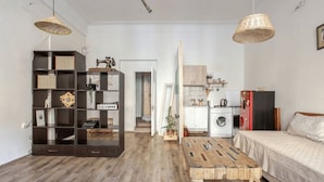 A compact living space with a wooden floor, a bed, a dining table, a built-in bookshelf, a washing machine, and a kitchenette. - Nice apartment with WiFi in charming T'bilisi (T'bilisi)
