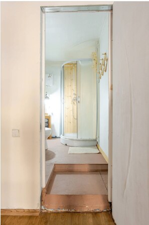 A narrow hallway leading to a bathroom with a shower, toilet, and sink.