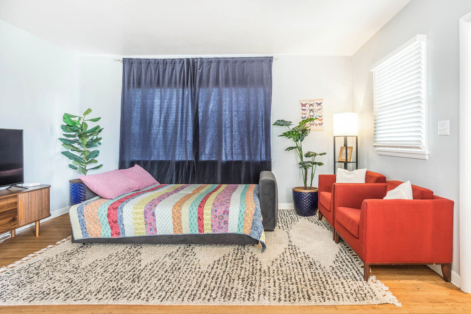 A modern bedroom with a bed, a red sofa, a TV, and a large window with curtains.