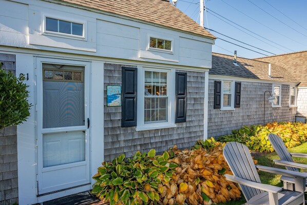 A two-story house with a front door, a welcome sign, and a chair in the yard.