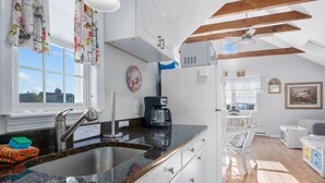 A modern kitchen with a granite countertop, stainless steel sink, and a coffee maker. - Seaflower – Where the Sea Meets Serenity (South Yarmouth)