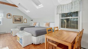 A bedroom with two beds, a dining table, and a large window with a view. - Seaflower – Where the Sea Meets Serenity (South Yarmouth)