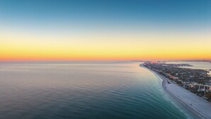 Un paisaje urbano costero al atardecer, con una playa extensa y una zona urbana densa en el fondo.