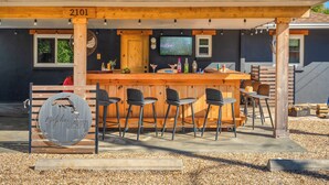 Un área de bar al aire libre con una barra de madera, taburetes y una pantalla de televisión.