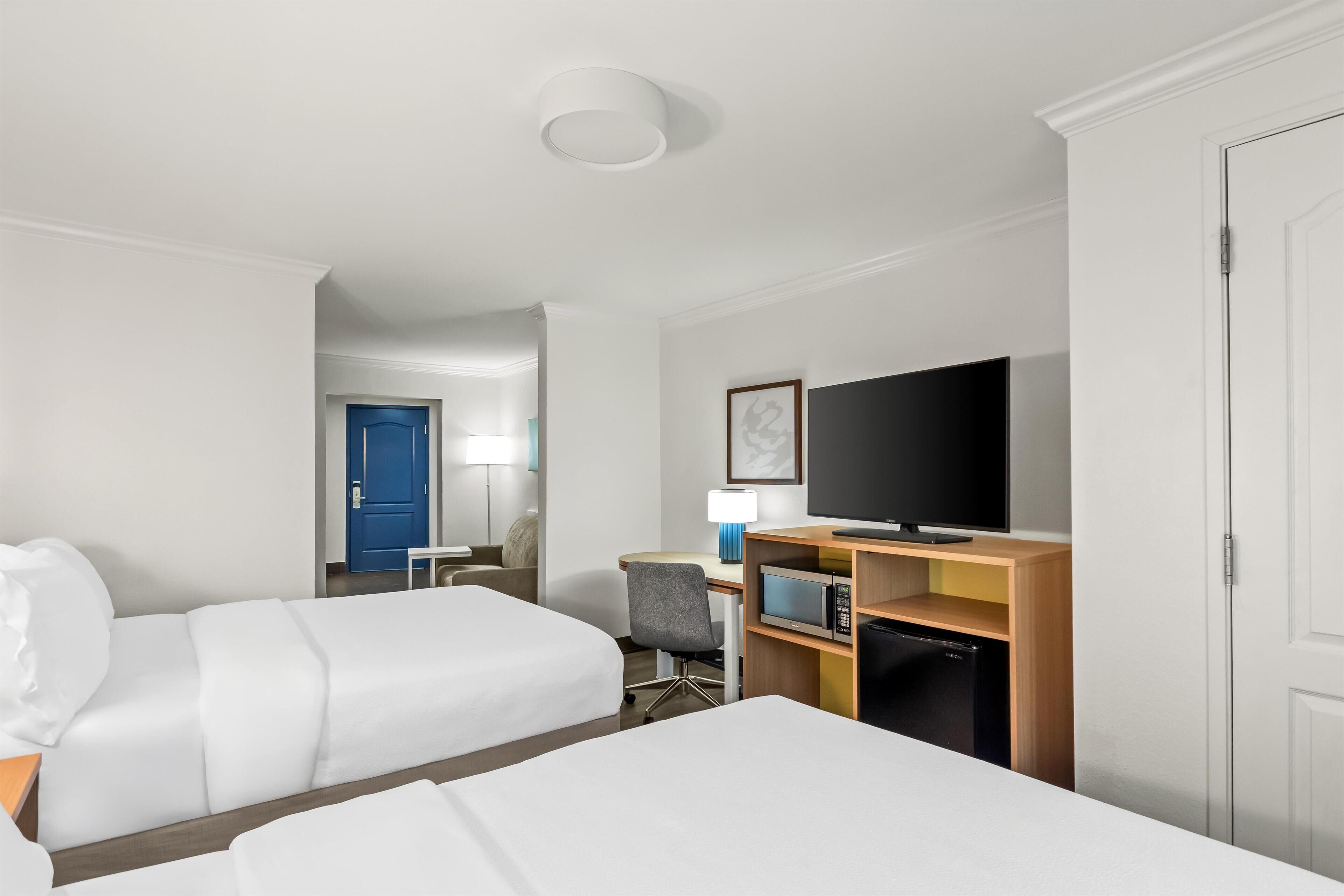 A hotel room with two beds, a desk with a computer, a television, and a microwave.