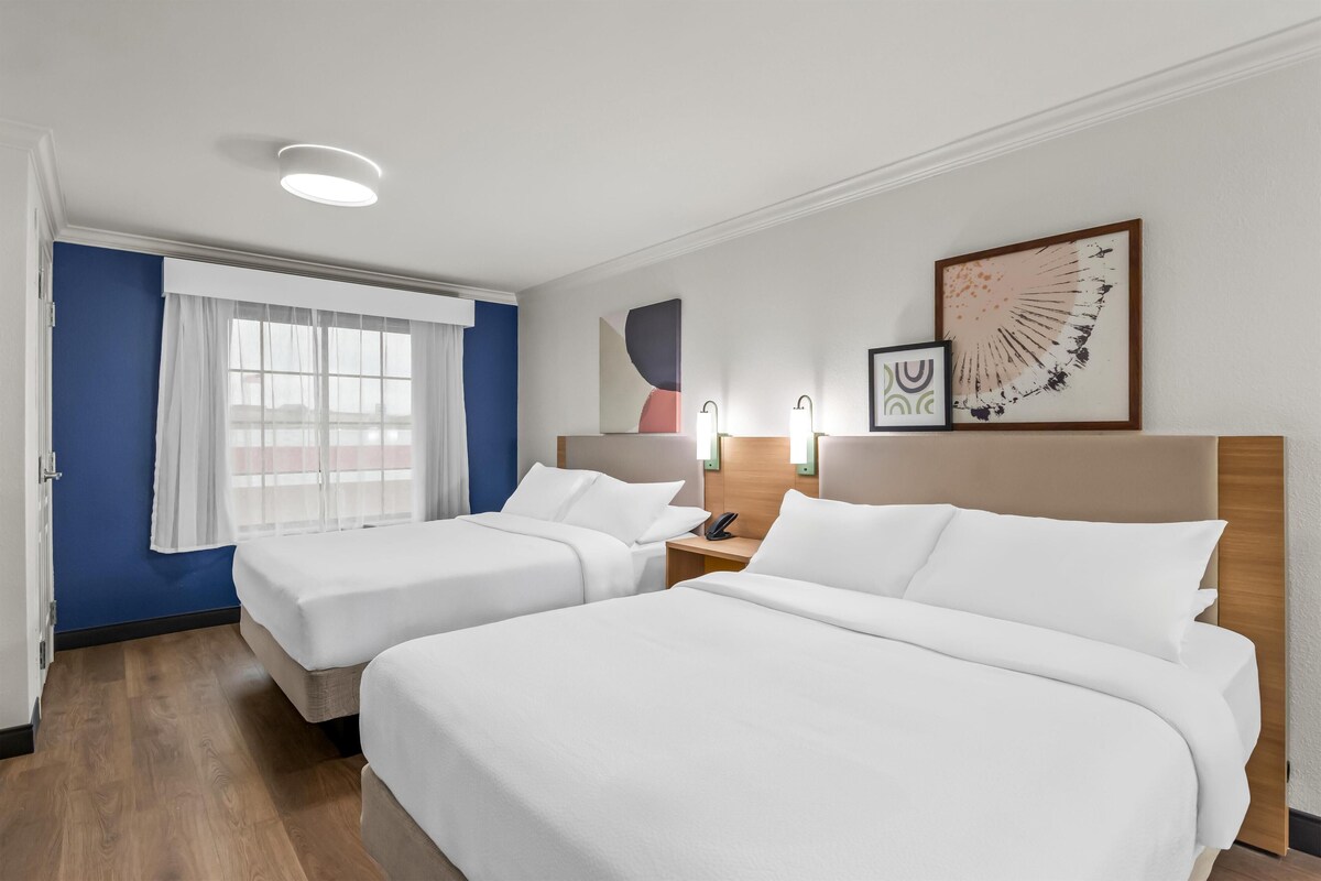Een hotelkamer met twee bedden, een raam met gordijnen, een telefoon aan de muur en abstracte kunst.