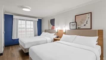 A hotel room with two beds, a window with curtains, a wall-mounted phone, and abstract art.
