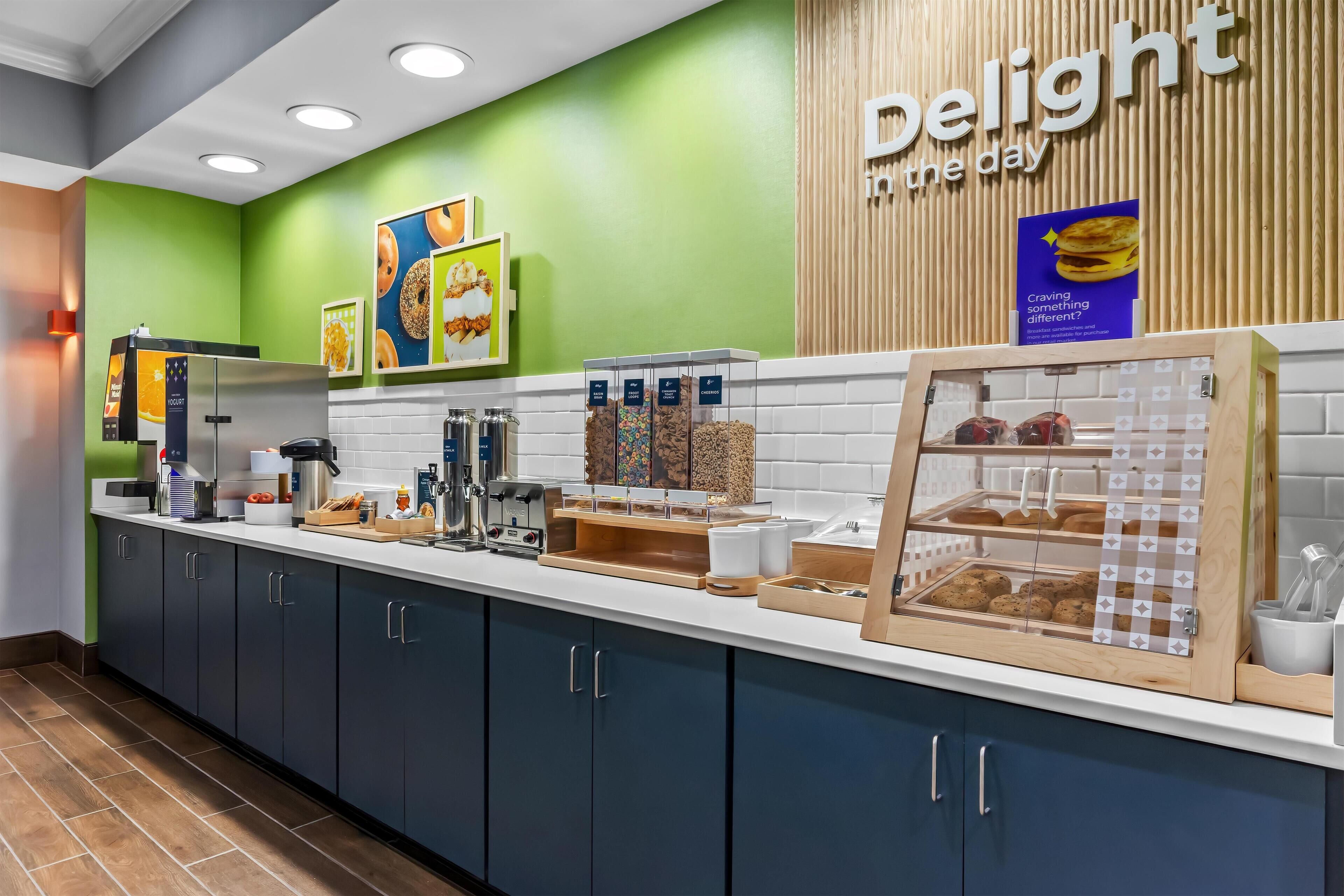 Un área de cocina moderna con una pared verde, un letrero que dice "delight the day" y diversos alimentos exhibidos en la encimera.