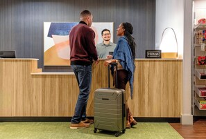 A reception desk with a wooden finish, a digital screen displaying a blurred face, and a sign indicating 'Hilton Honors'. - Spark by Hilton Cincinnati Fairfield (Cincinnati)