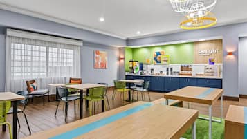 A modern dining area with wooden tables and chairs, a counter with food items, and a green wall with the text "Delight in the day".