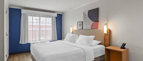 A hotel room with a bed, bedside tables, a window with curtains, and a wall-mounted artwork.
