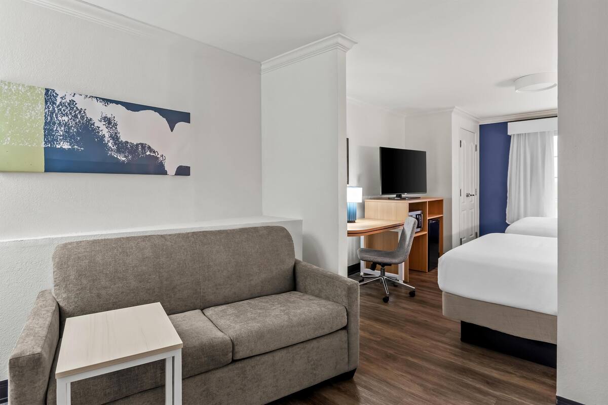 Et hotelværelse med sofa, lille bord, skrivebord med stol, fjernsyn og seng.