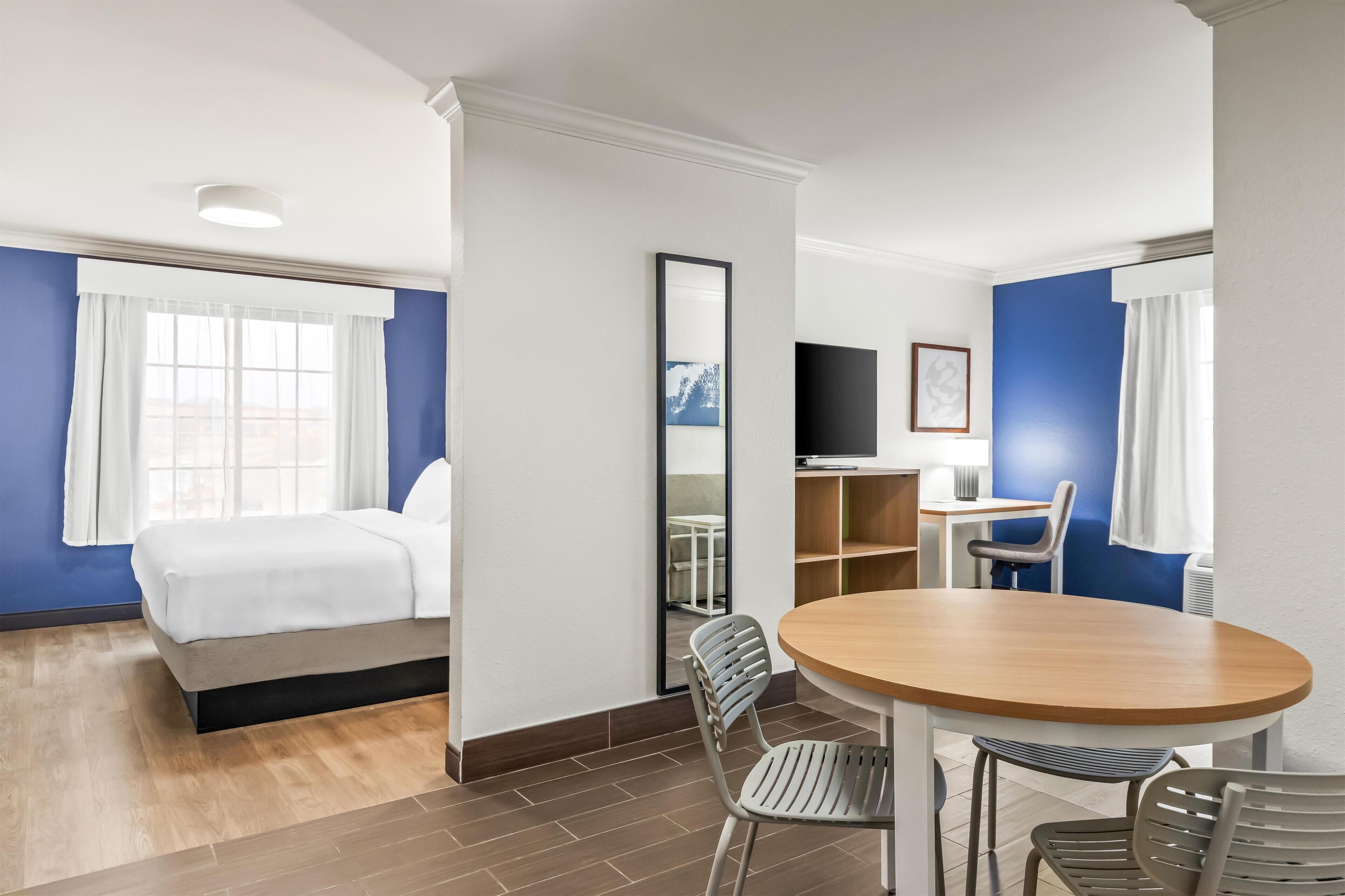 A hotel room with a bed, a desk with a chair, a round table with chairs, and a TV on the wall.