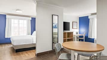Une chambre d’hôtel comprenant un lit, un bureau avec une chaise, une table ronde avec des chaises et un téléviseur fixé au mur.