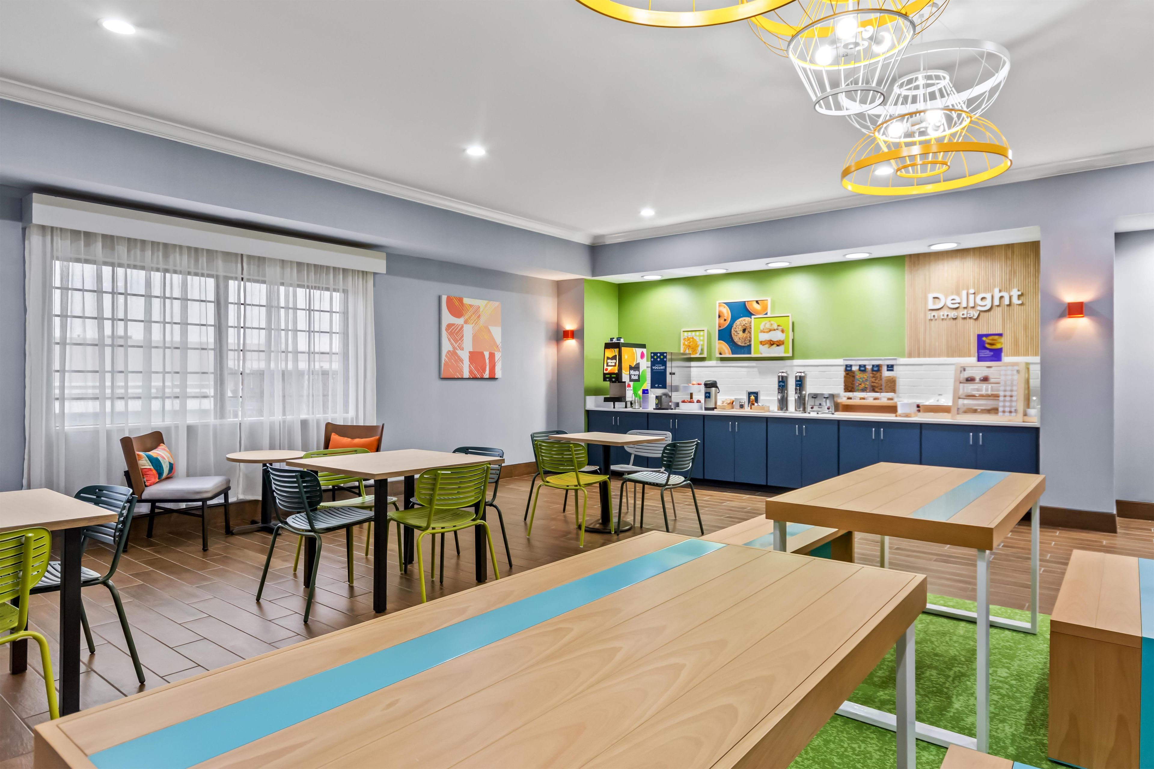A modern dining area with tables and chairs, a kitchen area with a counter, and a wall with a sign.