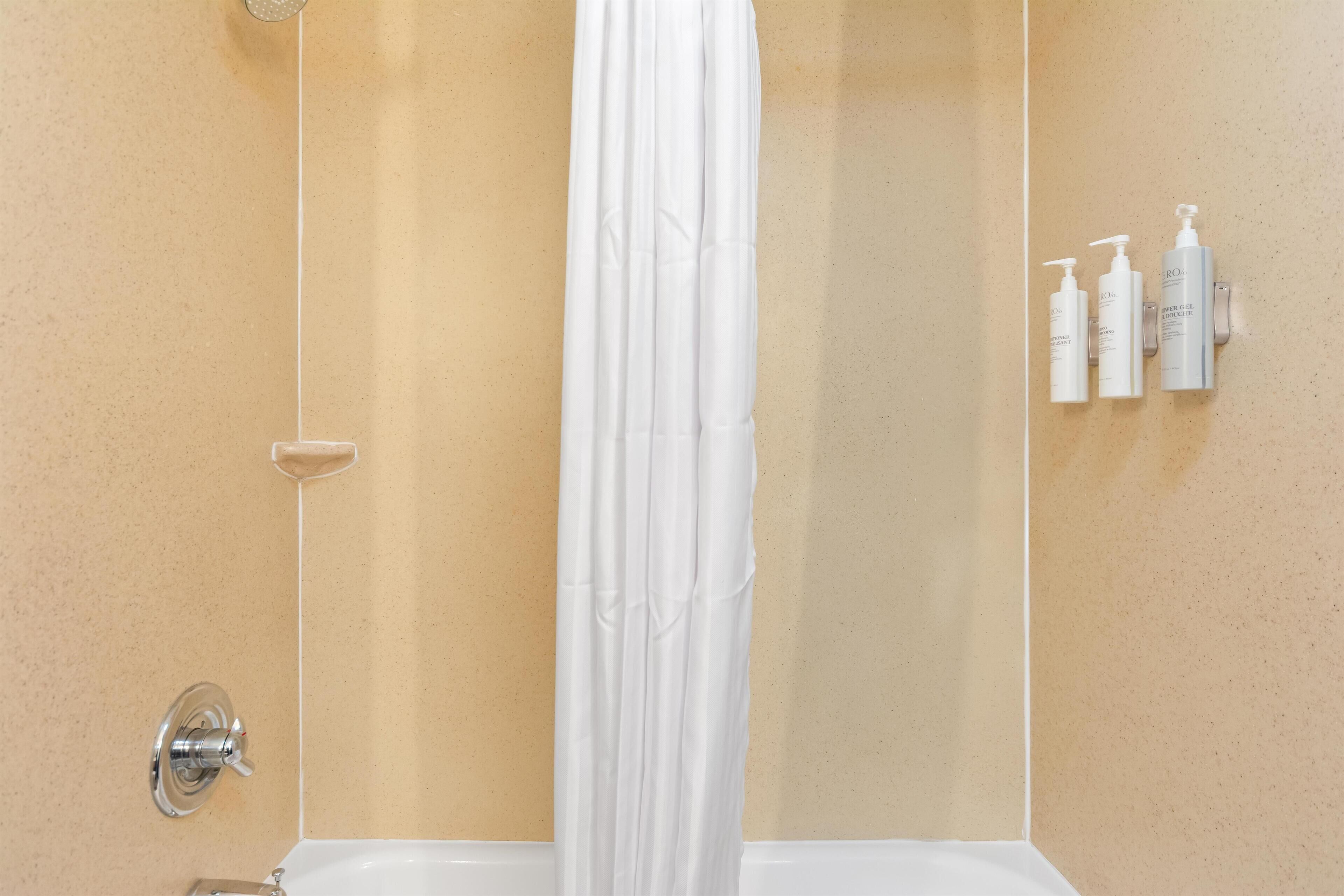Een badkamer met douchegordijn, douchehouder en drie flessen shampoo en conditioner aan de muur.